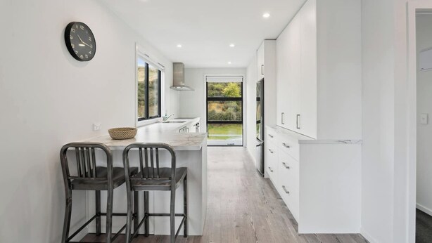 A modern kitchen with white cabinetry, a marble countertop, and two black chairs.