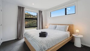 A bedroom with a bed, two bedside tables, a window, and a view of the outdoors.