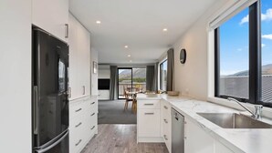 A modern kitchen with white cabinetry, a black refrigerator, and a large window offering a view of the outdoors.