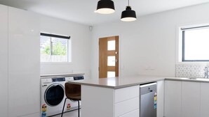 Una cucina moderna con mobili bianchi, lavatrice integrata, lavastoviglie e luci a sospensione.