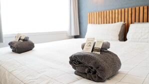 Un letto rifatto con una testiera, due asciugamani con etichette e una finestra con tende.
