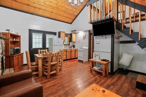 Un vaste espace de vie doté d’un plafond en bois, d’une table à manger avec des chaises, d’une cuisine équipée d’appareils modernes et d’un escalier avec des rampes en bois.