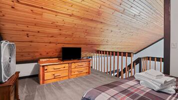 Ein Schlafzimmer mit Holzboden, einem Fernseher auf einer Kommode, einem Ventilator, einem Bett mit kariertem Überwurf und einer Treppe.