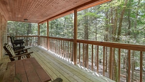 A wooden deck with benches and a table, overlooking a forest.
