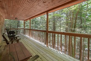 A wooden deck with benches and a table, overlooking a forest.
