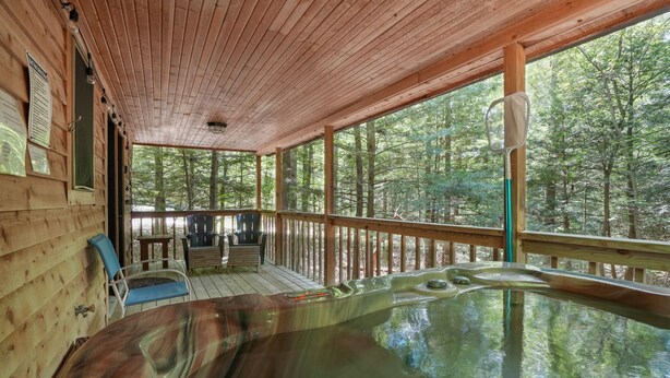 A wooden cabin with a hot tub, wooden deck, and a view of the forest.