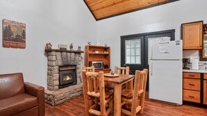 A cozy cabin interior with a stone fireplace, wooden dining table, and a kitchenette.