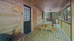 A wooden cabin with a porch, a welcome sign, a bench, and a picnic table.