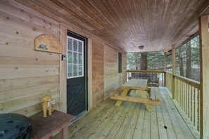 Una cabaña de madera con un porche, un letrero de bienvenida, un banco y una mesa de picnic.