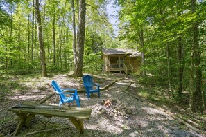 A rustic cabin with a fire pit and two blue chairs in a forest setting.
