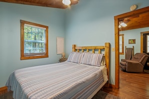 A bedroom with a bed, a window with blinds, a chair, and a wooden ceiling.