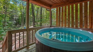 Ein Whirlpool auf einer Holzterrasse, umgeben von einem Wald.