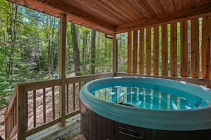 A hot tub in a wooden deck surrounded by a forest.