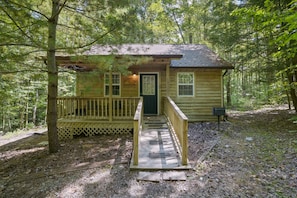 A wooden cabin with a front porch and a door, surrounded by trees.