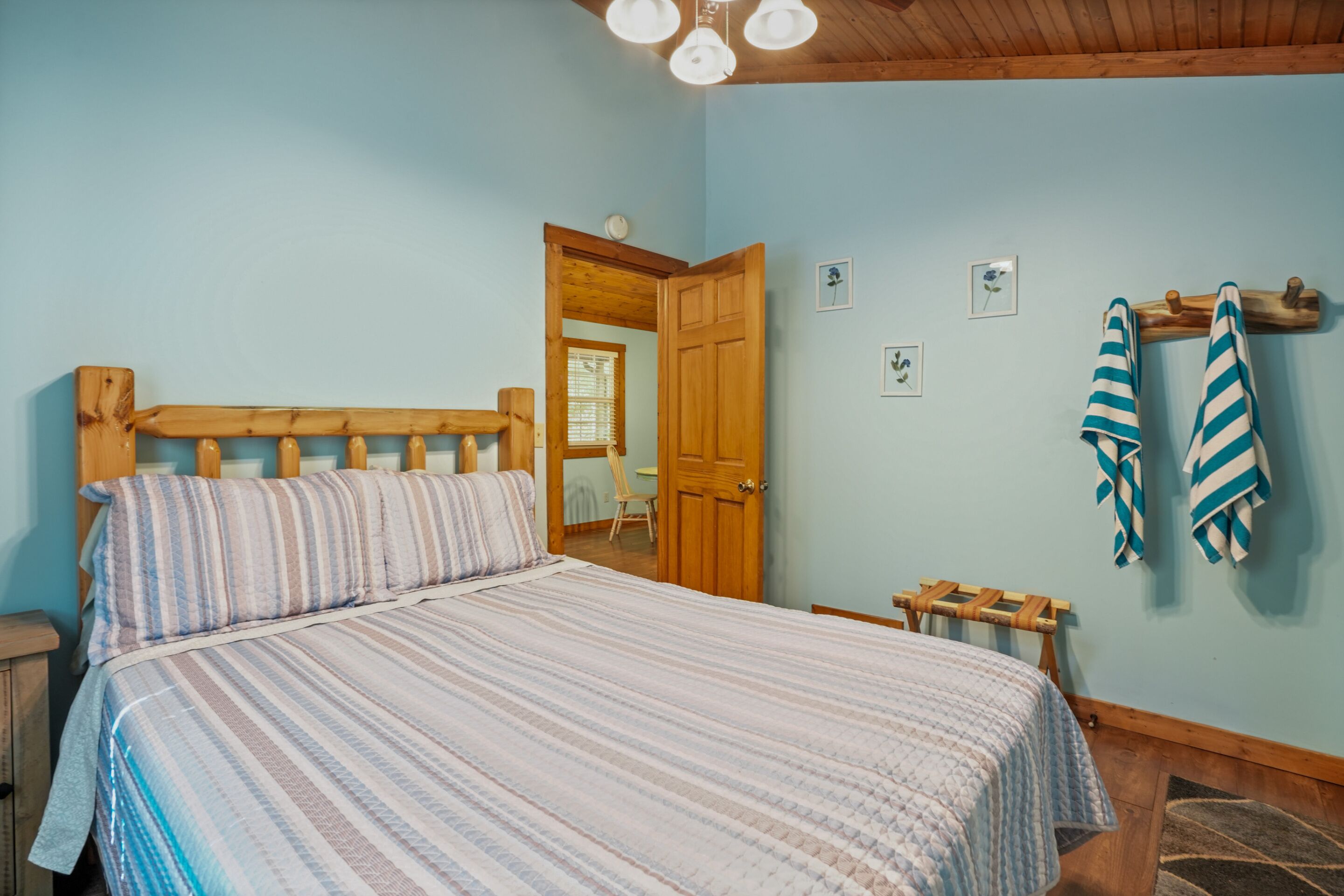 A bedroom with a wooden bed, a small bedside table, a wooden bench, and a door leading to another room.