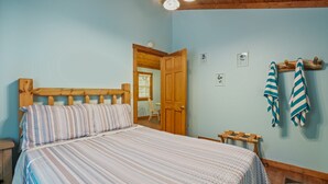 Un dormitorio con una cama de madera, una mesita de noche pequeña, un banco de madera y una puerta que da a otra habitación.