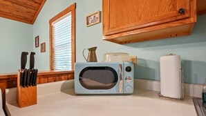 Una cocina con un microondas Galanz de estilo vintage, armarios de madera, un bloque de cuchillos, una jarra y un dispensador de toallas de papel.