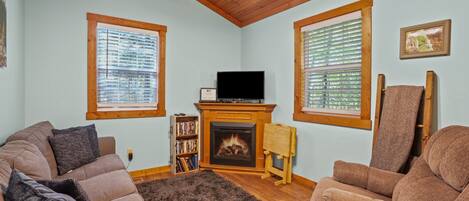 A cozy living room with a fireplace, two sofas, a bookshelf, and a television.