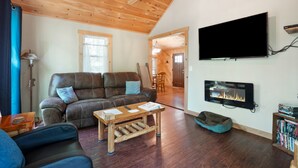 A cozy living room with a wooden ceiling, a flat-screen TV mounted on the wall, a fireplace, and a comfortable sofa. - Hidden Ridge Cabin | Big Pine Retreat, Trails (Rockbridge)