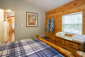 Une chambre dans une cabane en bois, avec un lit, une commode et une fenêtre.