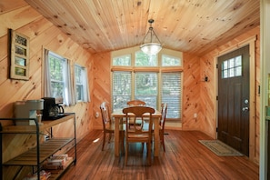 L’intérieur d’un chalet en bois comprend une table à manger, des chaises, une machine à café et une fenêtre avec des stores.