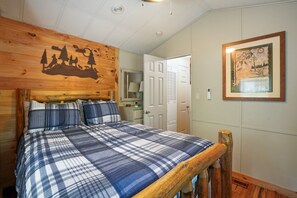 Une chambre à coucher avec une tête de lit en bois, une couvre-lit à carreaux et un tableau encadré accroché au mur.
