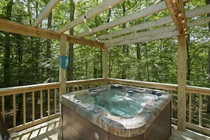 Un bain à remous sur une terrasse en bois, entouré d’une forêt.