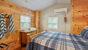 A wooden cabin-style bedroom with a bed, a dresser, a window with blinds, an air conditioning unit, and a hanging light fixture. - Hidden Ridge Cabin | Big Pine Retreat, Trails (Rockbridge)