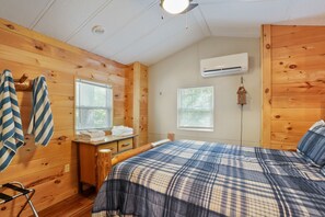 A wooden cabin room with a bed, a dresser, a window, and an air conditioning unit. - Hidden Ridge Cabin | Big Pine Retreat, Trails (Rockbridge)