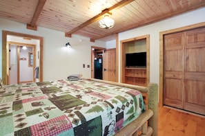 A cozy room with a wooden ceiling, a quilted bedspread, a television, and a wooden wardrobe. - Hummingbird Lodge at Big Pine Retreat, Indoor Pool (Rockbridge)