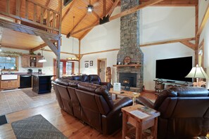 Amplia sala de estar con sofás de cuero, chimenea de piedra y televisor.