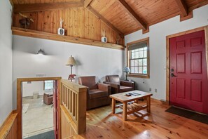 A wooden-floored living room with two leather sofas, a wooden coffee table, and a red door. - Hummingbird Lodge at Big Pine Retreat, Indoor Pool (Rockbridge)