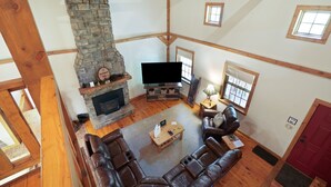 A spacious living room with a stone fireplace, leather sofas, a flat-screen TV, and wooden beams.