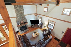 A spacious living room with a stone fireplace, leather sofas, a flat-screen TV, and wooden beams. - Hummingbird Lodge at Big Pine Retreat, Indoor Pool (Rockbridge)