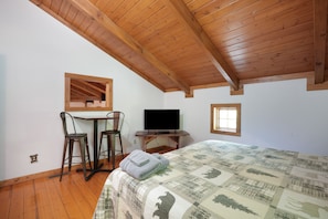 Ein Schlafzimmer mit Holzboden, einem Bett mit Steppdecke, einem Schreibtisch mit Fernseher und zwei Stühlen.