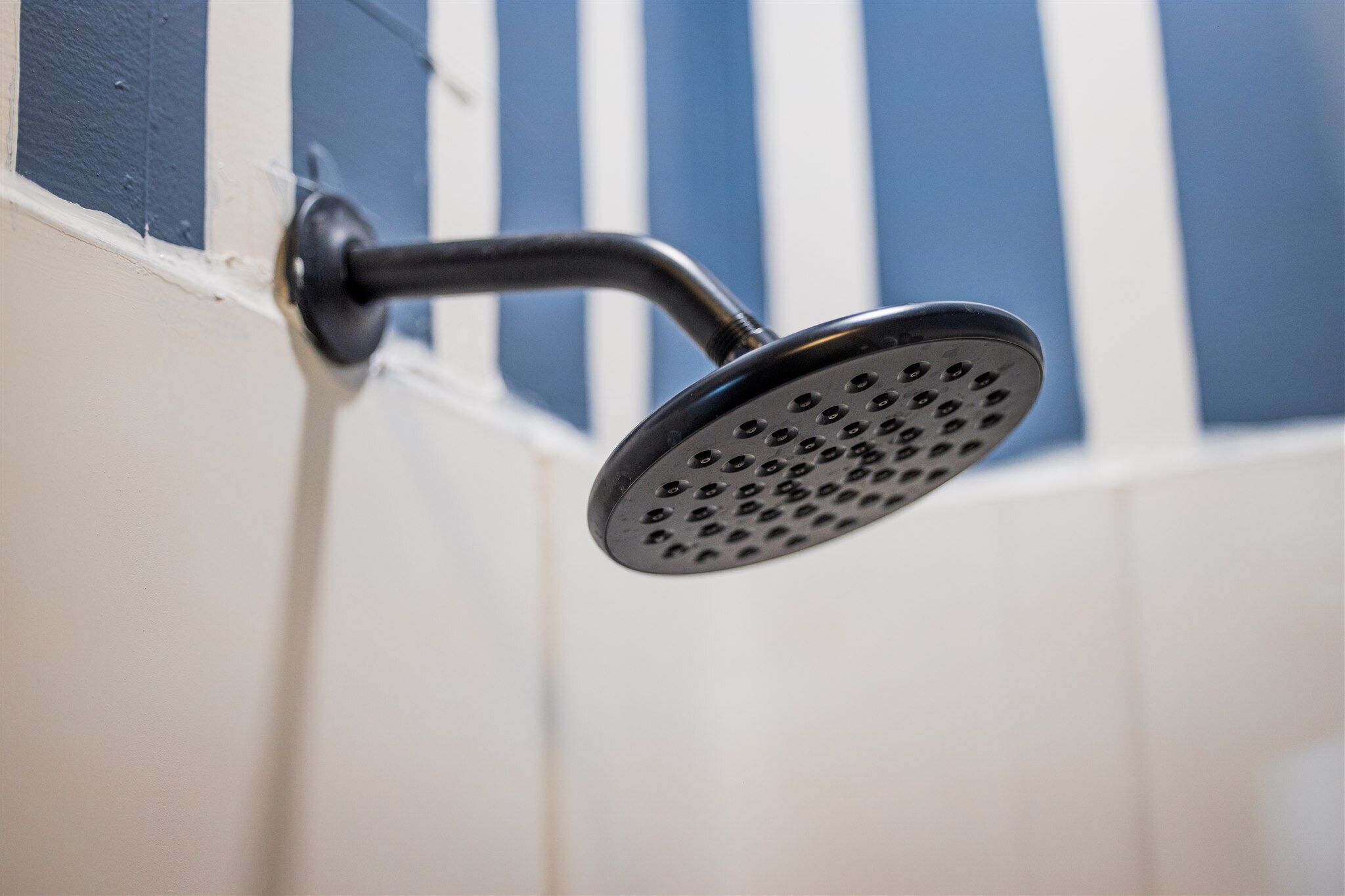 A showerhead with a curved handle, mounted on a wall with blue and white stripes.
