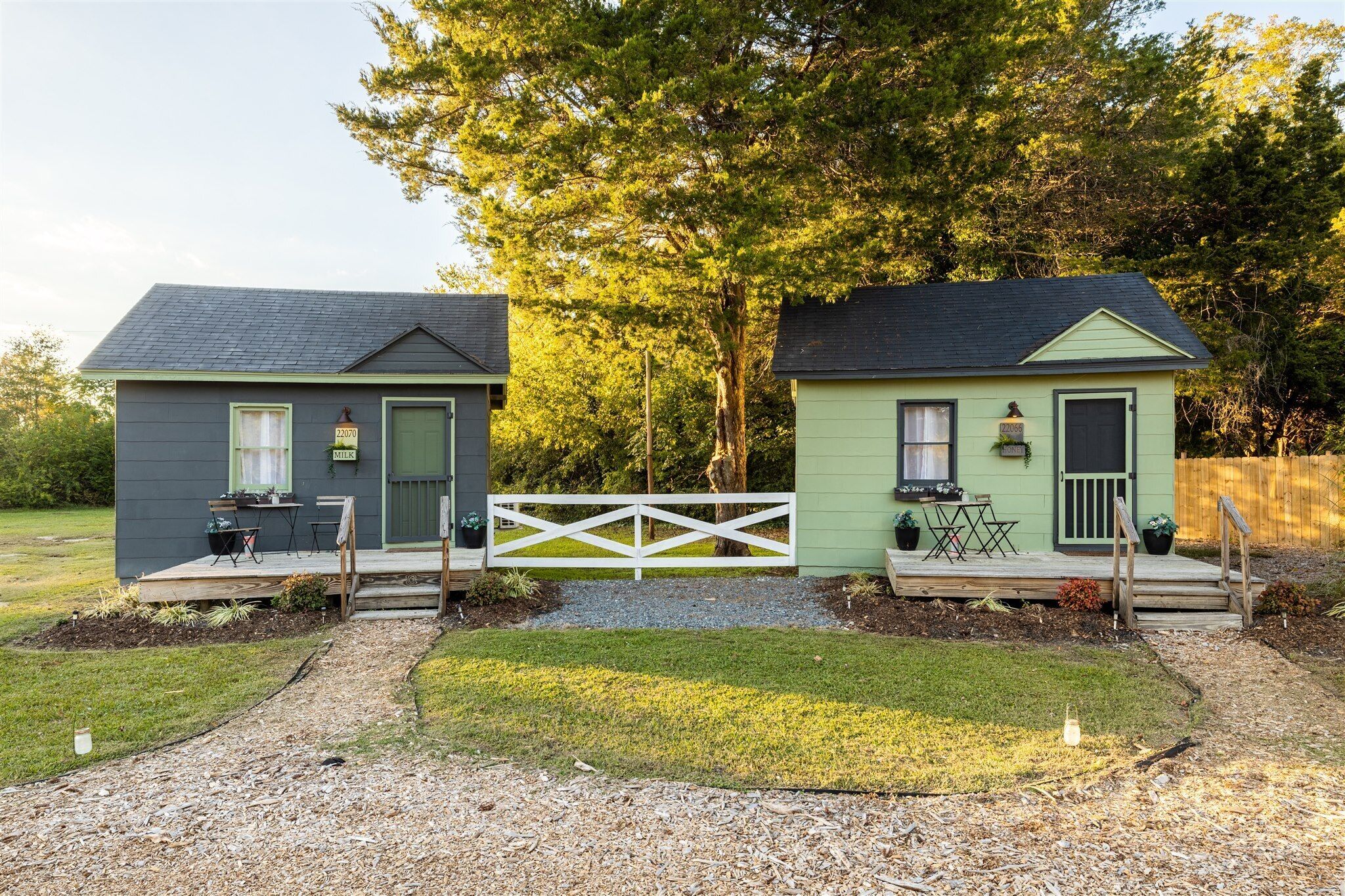 Two small, single-story houses with green and gray exteriors, each with a front porch and a small deck.
