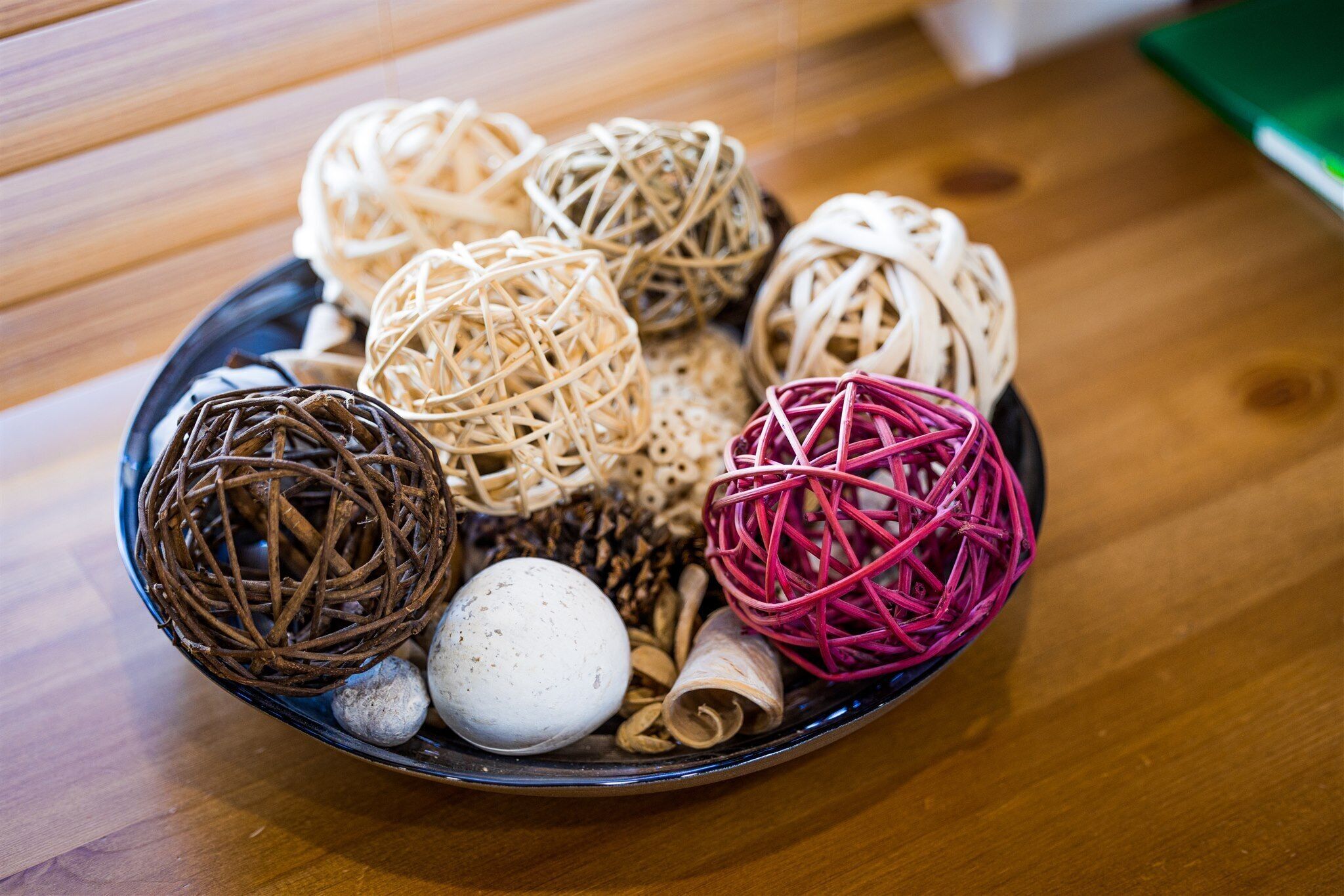 A bowl containing various woven balls and a white egg on a wooden table.