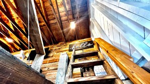 Una escalera de madera con un cartel que dice 'hello' en la parte superior, que lleva a una habitación con paredes de madera y techo inclinado.