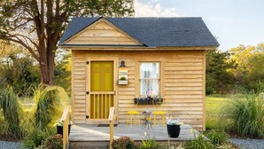 Una pequeña cabaña de madera con puerta amarilla, buzón y un letrero que dice "22086 Vintage".