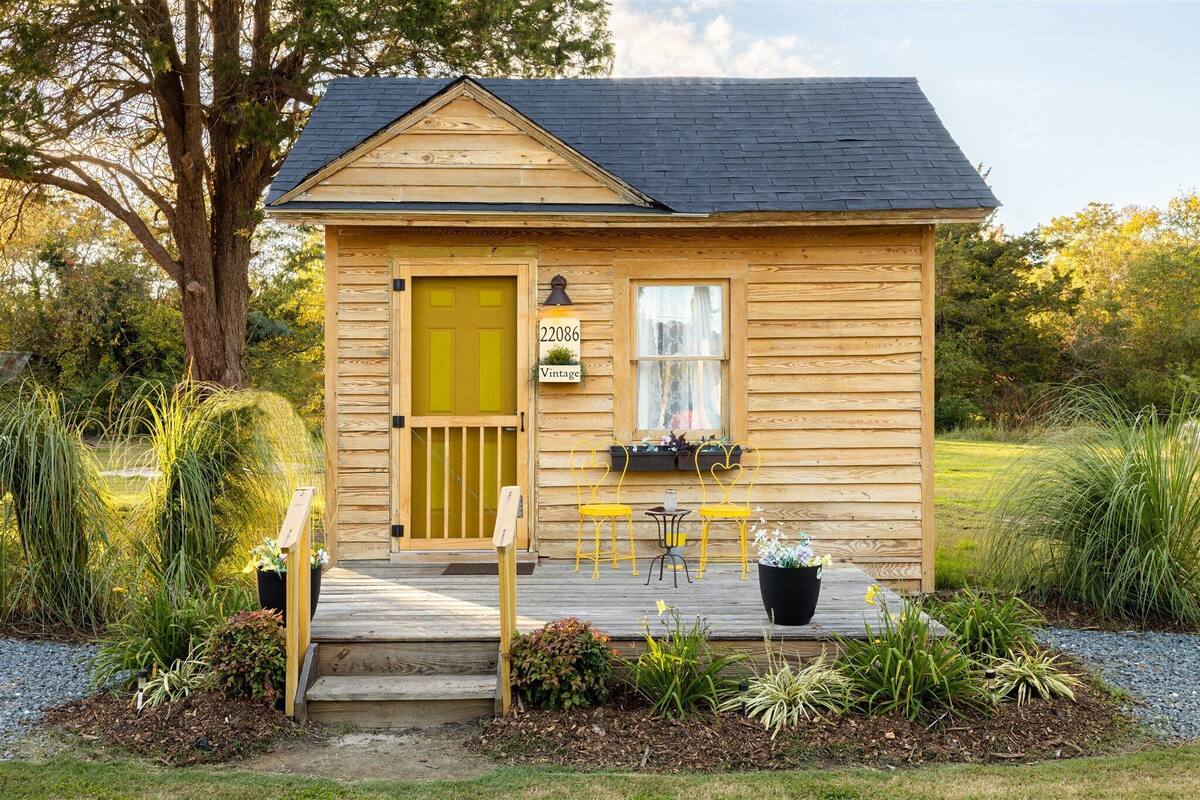Une petite cabane en bois avec une porte jaune, une boîte aux lettres et une pancarte indiquant « 22086 Vintage ».