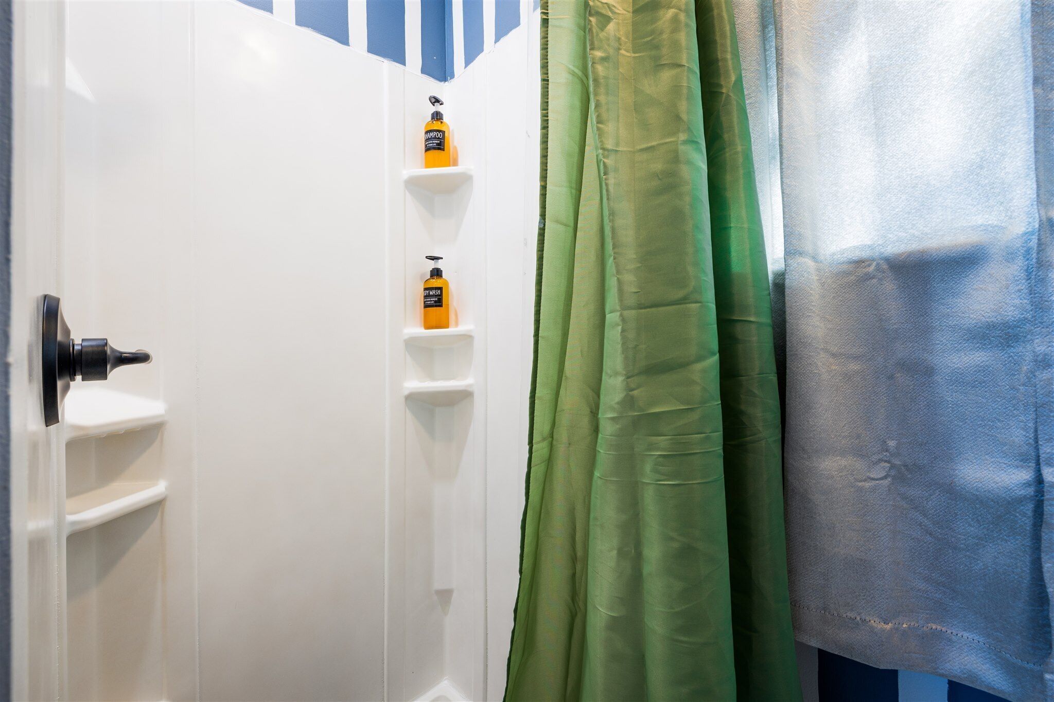 Un baño con una puerta blanca, cortina de ducha verde y un estante con dos botellas.