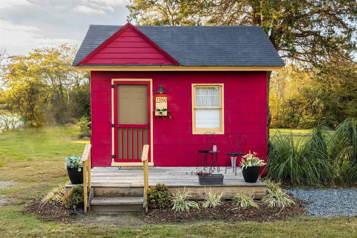 Une petite maison rouge avec un toit sombre, une porte d’entrée et un panneau indiquant le numéro de la maison.