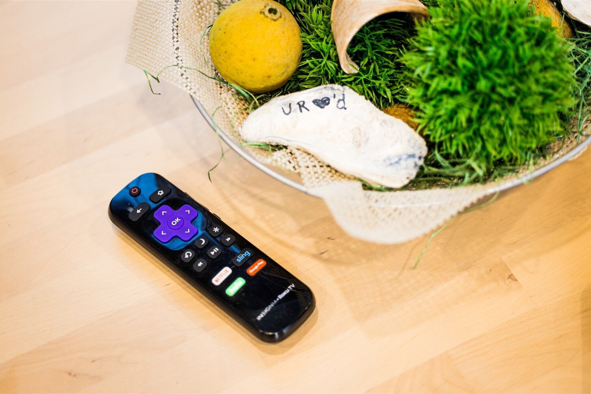 A remote control, a basket with a lemon, and a small plant on a wooden surface.