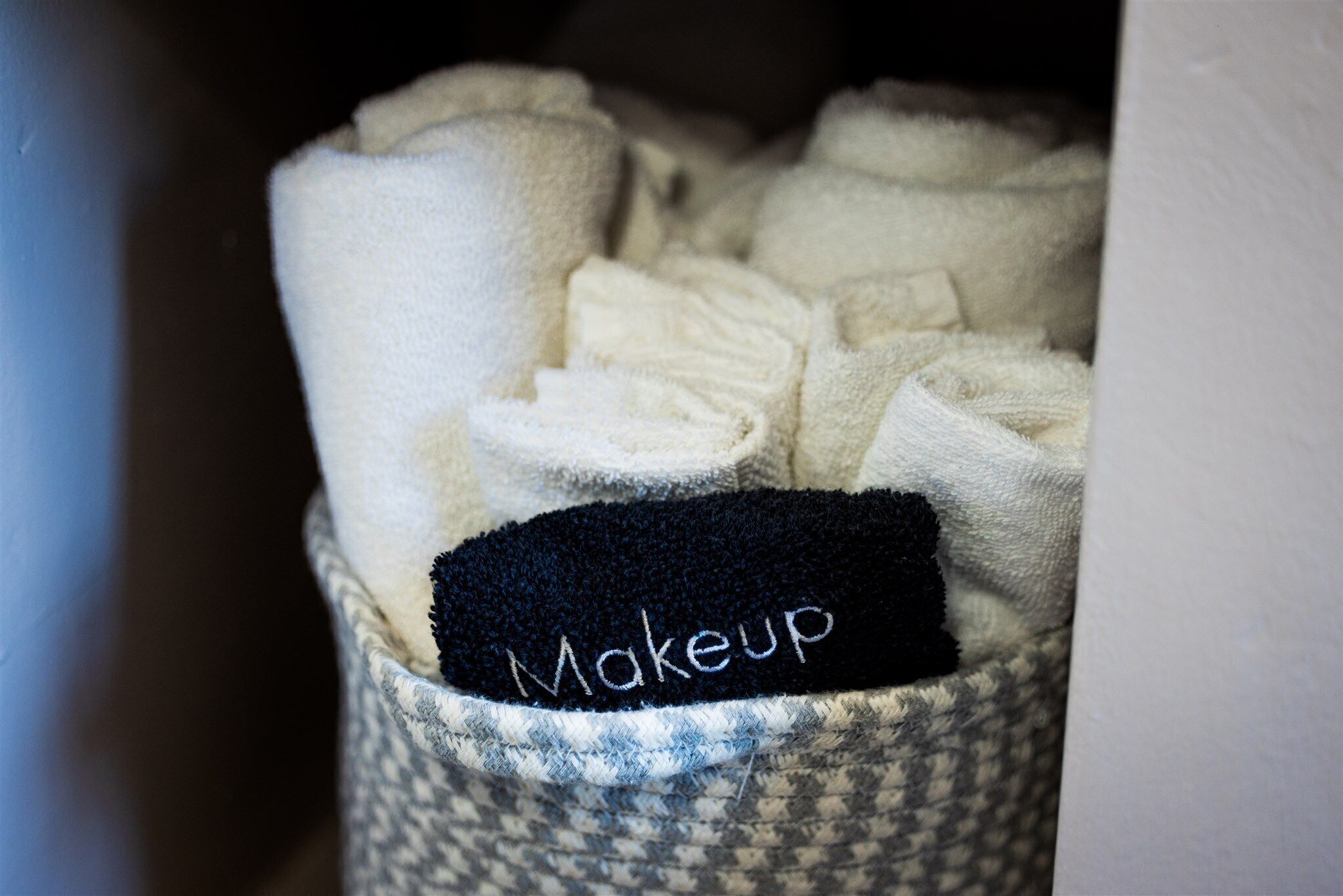 A storage bin filled with neatly folded towels, labeled with a black tag that reads "Makeup".