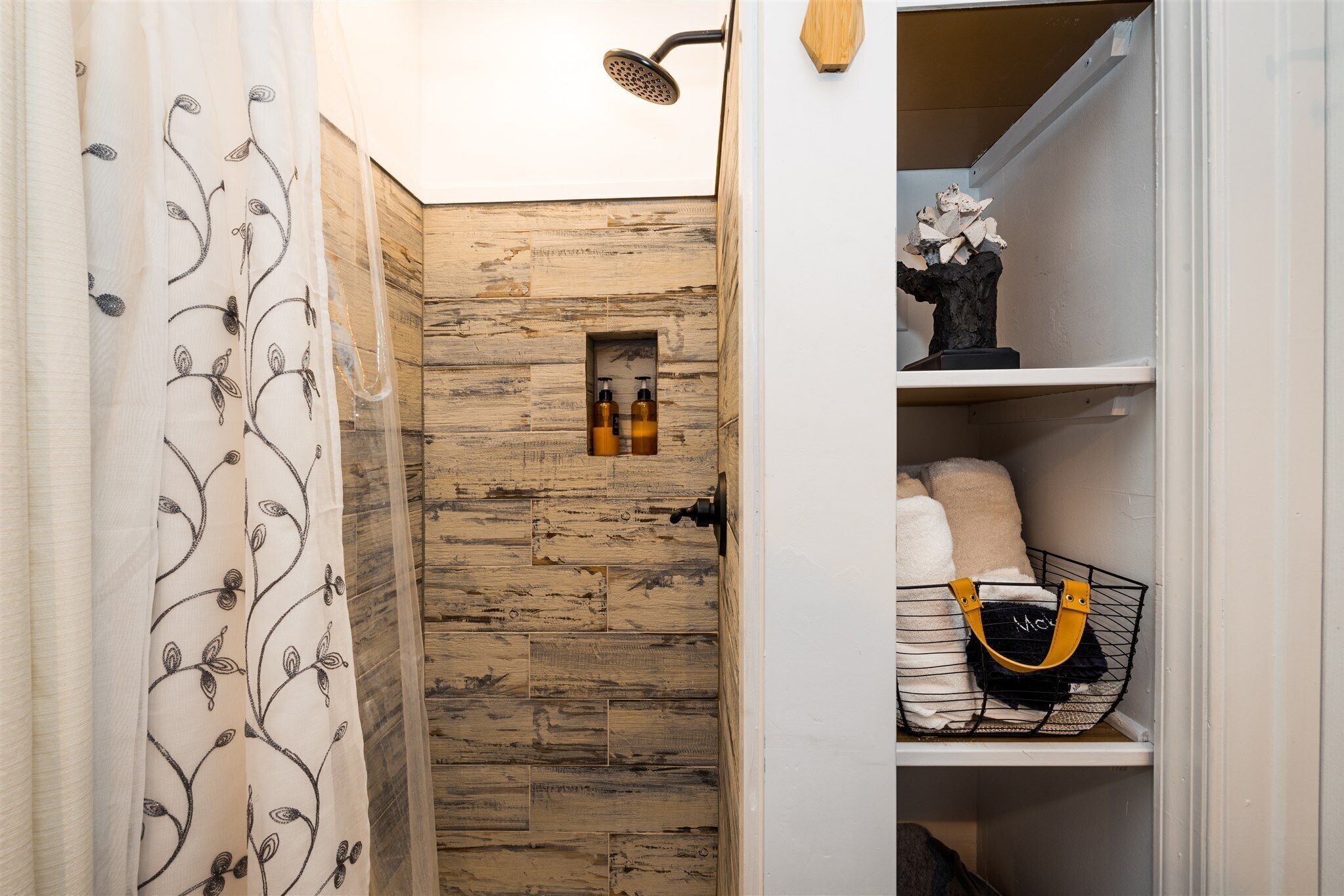 A bathroom with a wooden wall, a shower, and a shelf with toiletries and a decorative item.