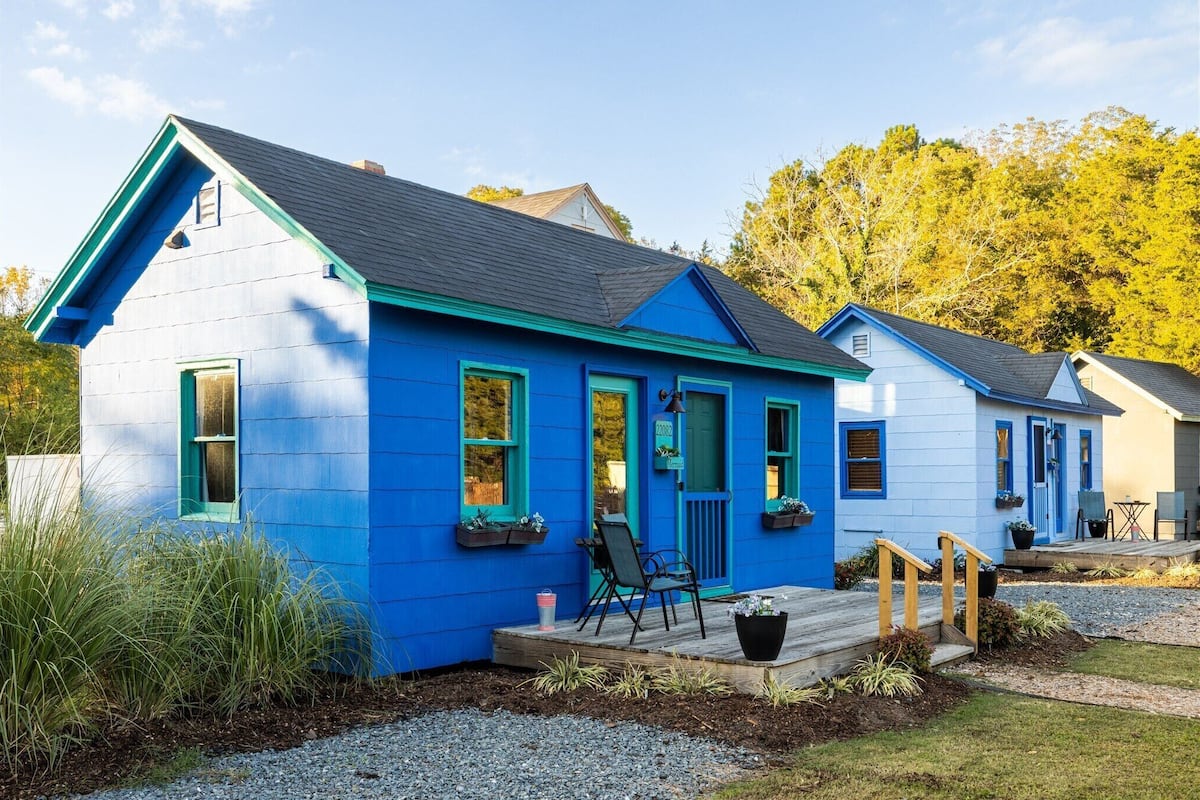 Une maison bleue avec un porche, une petite terrasse et une fenêtre ornée d’une plante.