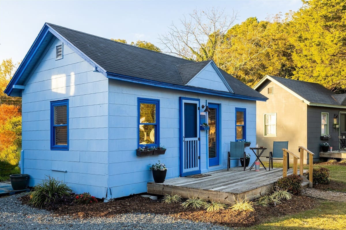 Une petite maison de plain-pied, à l’extérieur bleu, avec un porche à l’avant et une petite terrasse.