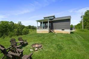 Een modern huis met een overdekte veranda, een vuurkorf en buitenmeubels.
