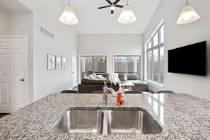 A modern kitchen with granite countertops, stainless steel sink, and pendant lighting.